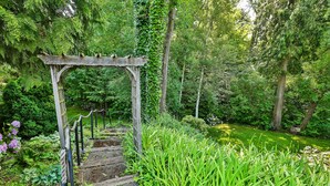A wooden pergola with a rope railing, surrounded by lush greenery and a garden path. - Brookside Bed & Breakfast (Hood River)