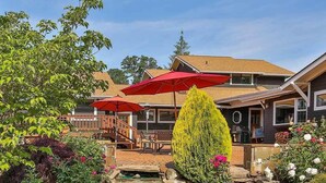 A backyard with a stone water feature, a wooden deck, and a red umbrella. - Brookside Bed & Breakfast (Hood River)