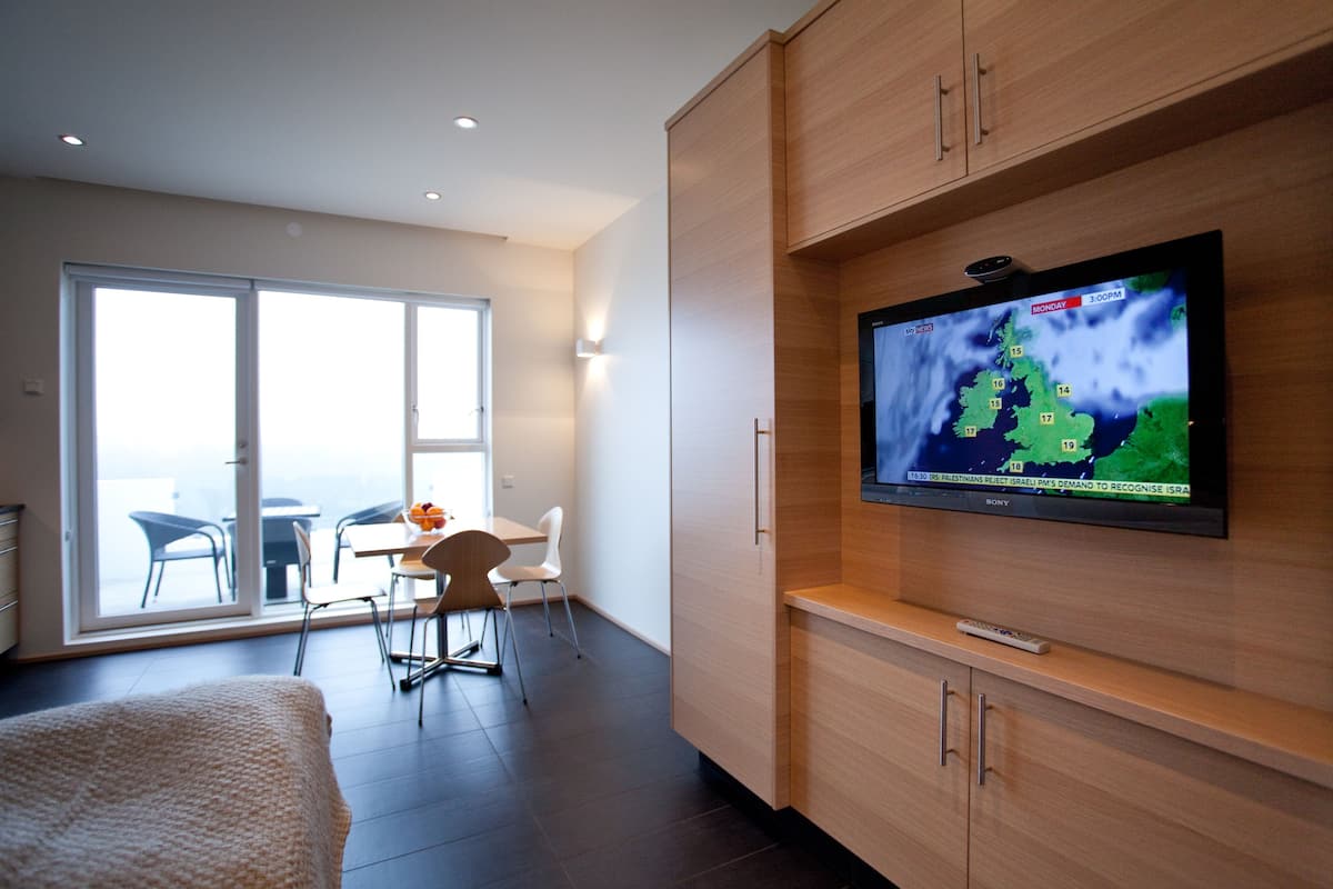 A modern hotel room with a large TV mounted on the wall displaying a weather forecast.