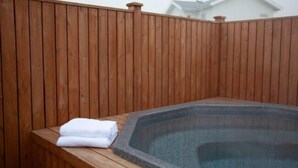 Jacuzzi amb un pont de fusta i vora de pedra, envoltat per una tanca de fusta.
