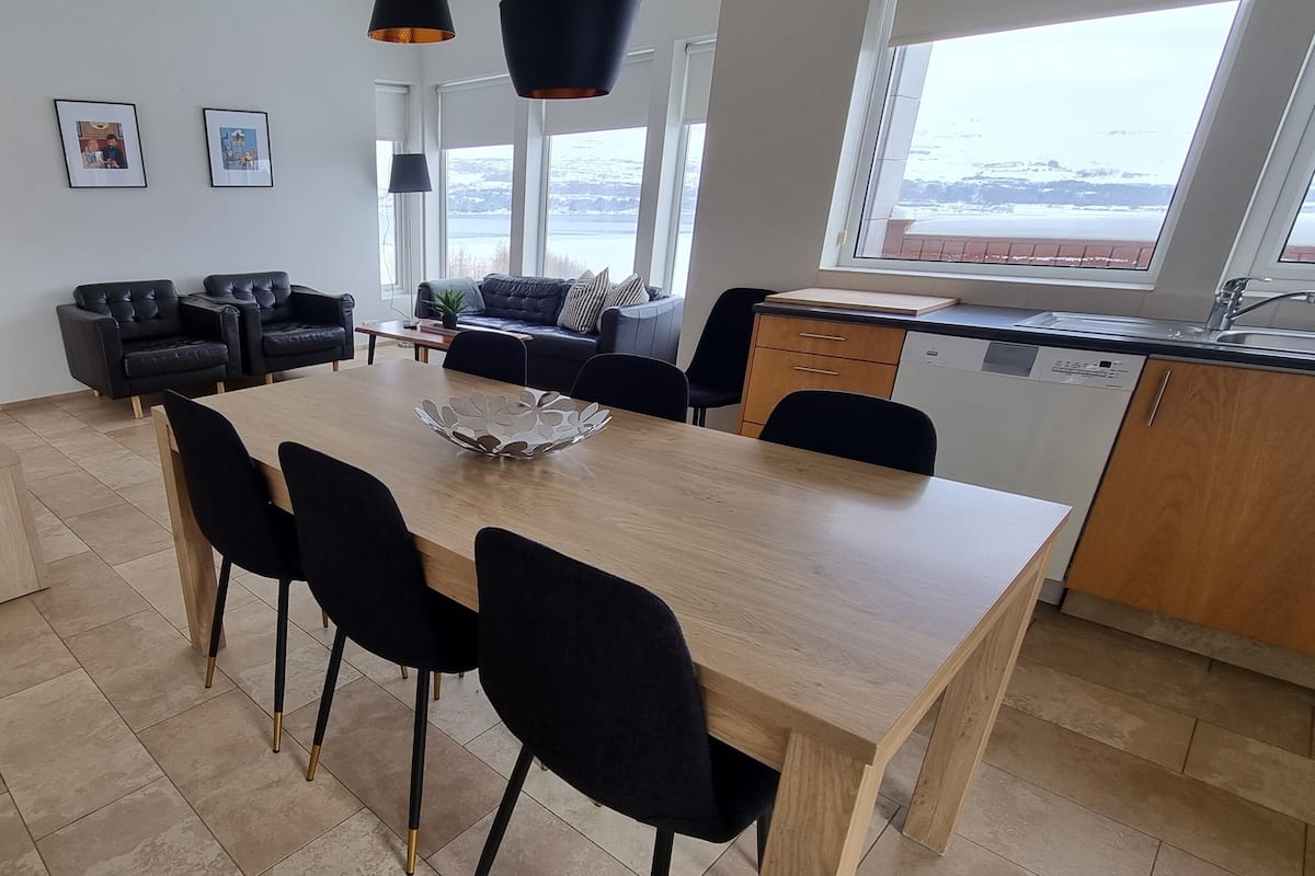 A modern kitchen with a dining area, large windows, and a view of the outdoors.