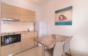 Une cuisine compacte avec des meubles en bois, un réfrigérateur blanc, un four encastré et un coin repas comprenant une table en bois et deux chaises.