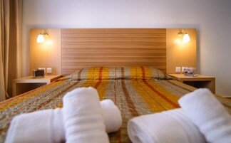 Una habitación de hotel con una cama, dos mesitas de noche y dos lámparas fijadas a la pared.