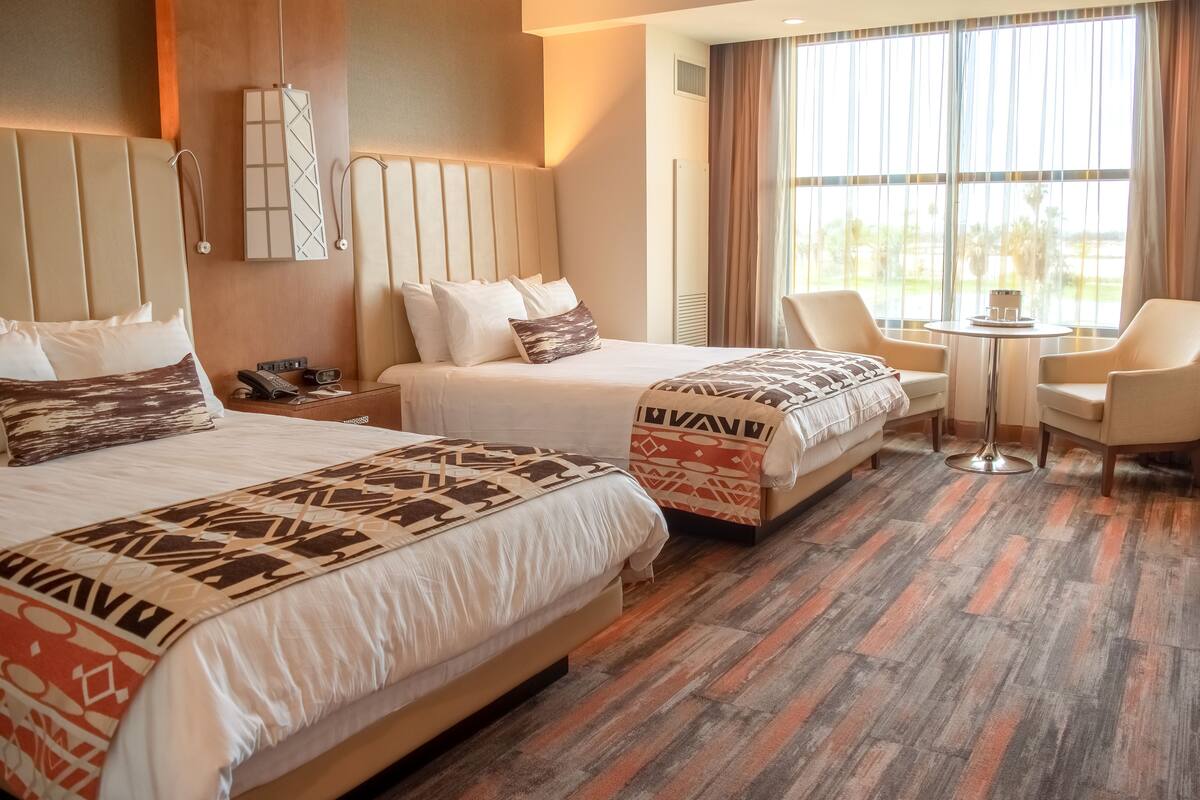 Una habitación de hotel con dos camas, una mesita y una silla.