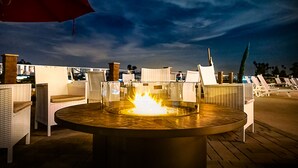 Un espace extérieur aménagé pour les soirées, avec un foyer central, des fauteuils confortables et un parasol rouge.