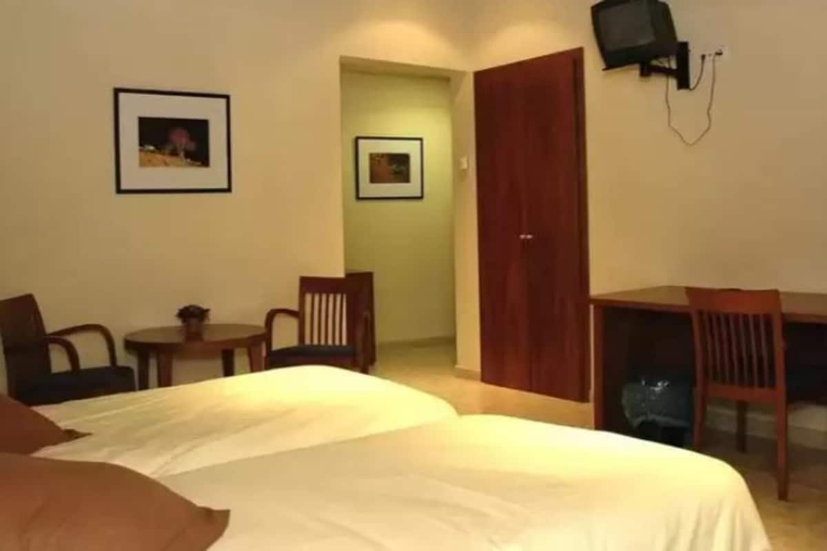 Habitación de hotel con cama, escritorio, dos sillas, televisor y dos cuadros en la pared.
