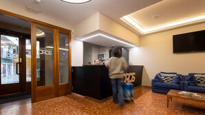 A hotel lobby with a reception desk, a blue sofa, and a television on the wall. - Hotel Oros by Nexta (Encamp)