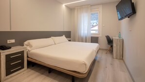 A modern hotel room with a large bed, bedside table, and a flat-screen TV mounted on the wall. - Hotel Oros by Nexta (Encamp)