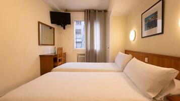 Habitación de hotel con dos camas, un televisor montado en la pared, una ventana con cortinas y un cuadro enmarcado en la pared.