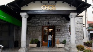 A hotel entrance with a stone facade, a sign reading "HOTEL OROS," and a person at the door. - Hotel Oros by Nexta (Encamp)