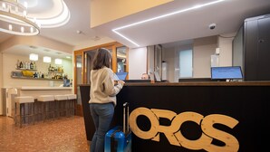 A reception area with a bar, a wooden sign with 'OROS', and a person with a suitcase. - Hotel Oros by Nexta (Encamp)