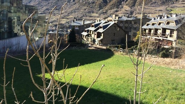 A rural village with traditional stone houses, a grassy field, and mountains in the background. - Hotel Oros by Nexta (Encamp)