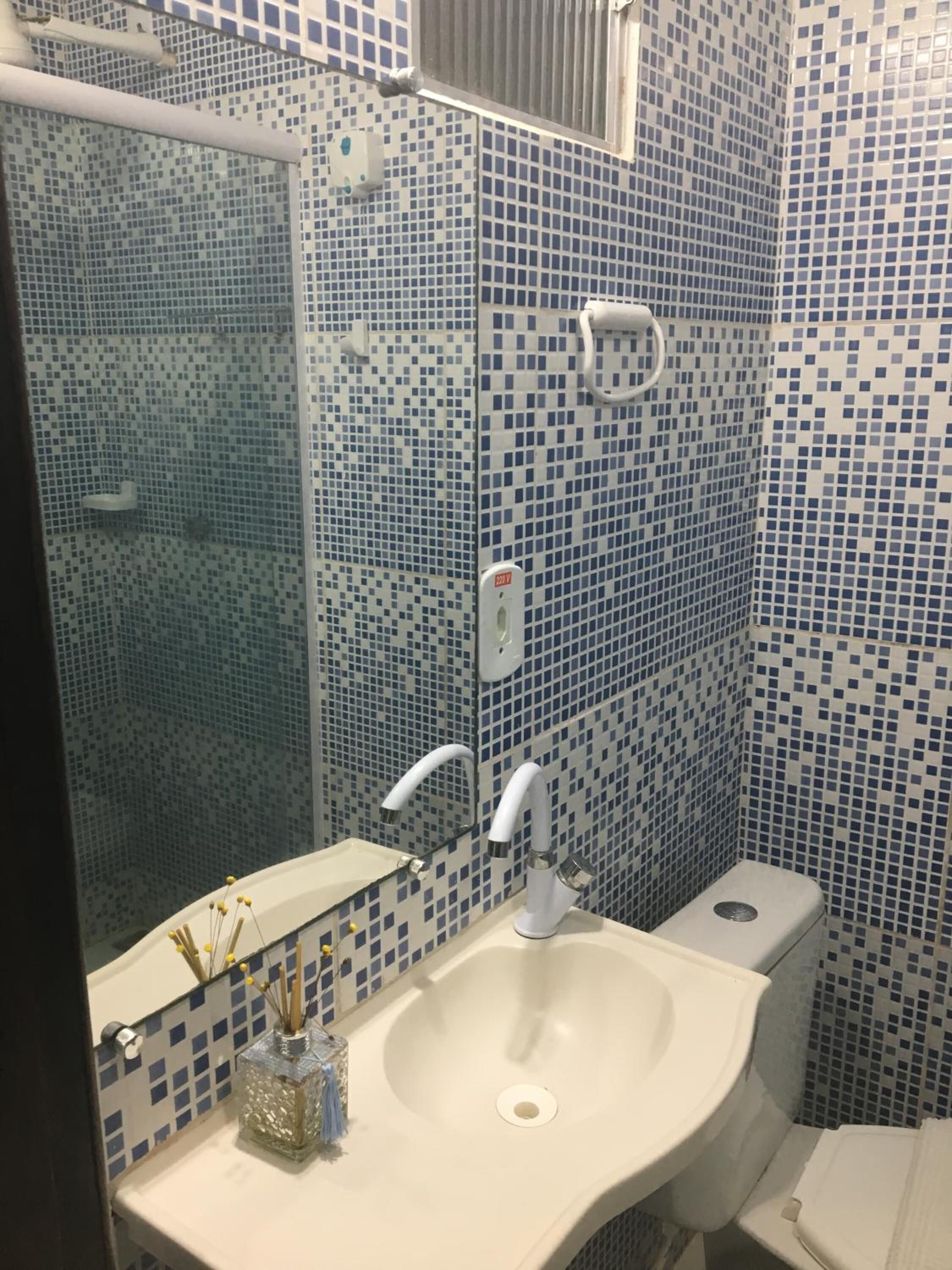 A bathroom with a sink, mirror, and toilet. The walls are tiled with a blue mosaic pattern.