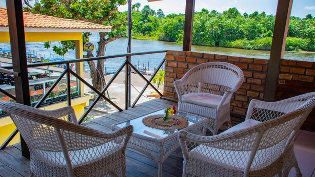 Un balcon agrémenté de meubles en osier et d’une table en verre, offrant une vue sur une rivière et une végétation luxuriante.