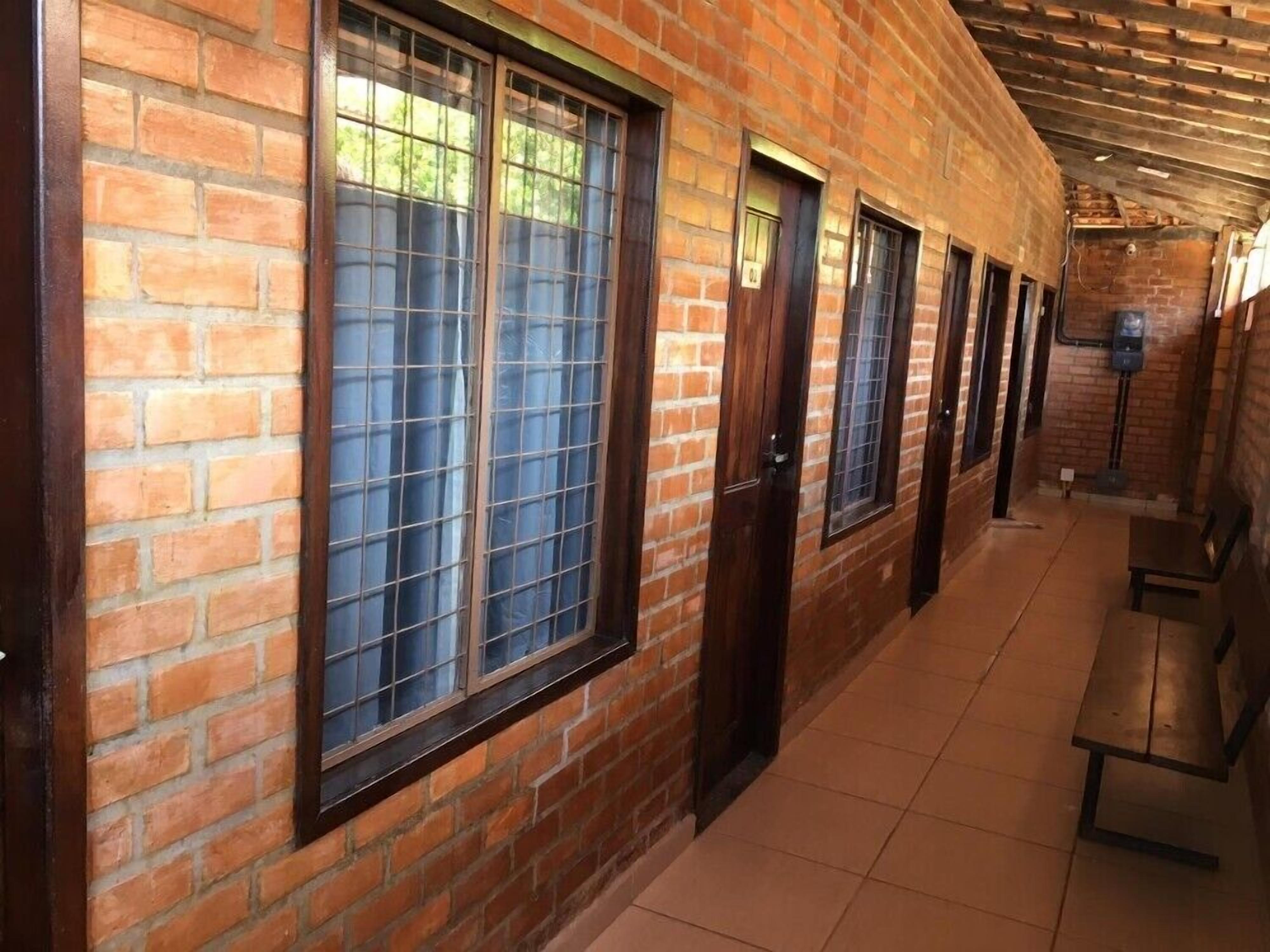 Un pasillo con paredes de ladrillo, ventanas amplias con rejas metálicas y suelo de baldosas.