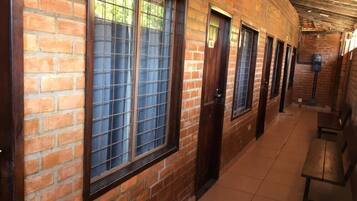 Un pasillo con paredes de ladrillo, ventanas amplias con rejas metálicas y suelo de baldosas.