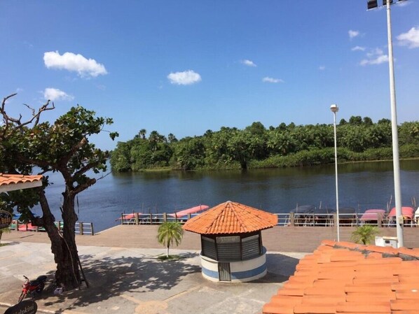 Vista al río con un pequeño pabellón, un árbol y una hilera de sombrillas rojas.