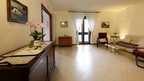 A living room with a sofa, armchairs, a coffee table, a wooden cabinet, a potted orchid, and a framed picture on the wall. - B&B La Stradella (Ostuni)