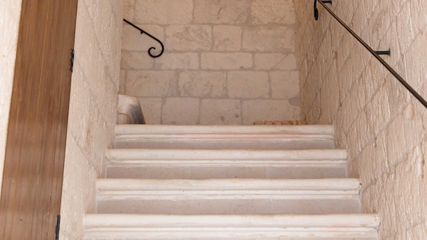 A staircase with white steps leading to a wooden door, flanked by textured white walls and a wall-mounted light fixture. - B&B La Stradella (Ostuni)