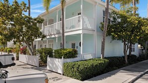 Een tweelaags huis met een balkon, omringd door palmbomen en een witte picket fence.