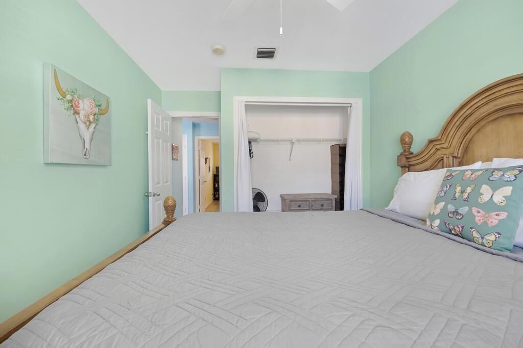 A bedroom with a large bed, a wooden headboard, a door leading to a bathroom, and a wall-mounted artwork.