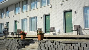 A row of hotel rooms with green doors numbered 14 to 15, outdoor seating with chairs, and potted plants. - Motel Quatre Saisons (Forestville)