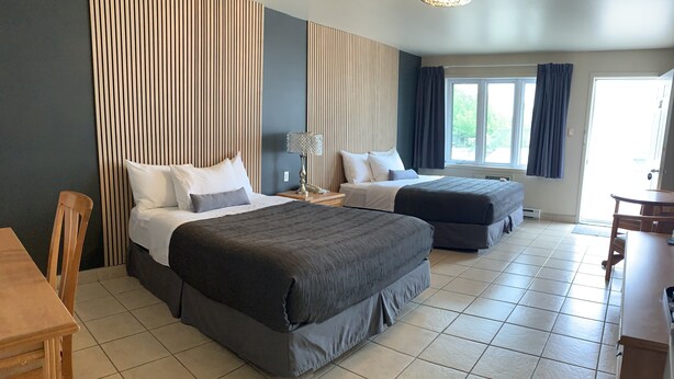 A hotel room with two beds, a dining table, and a window with curtains. - Motel Quatre Saisons (Forestville)