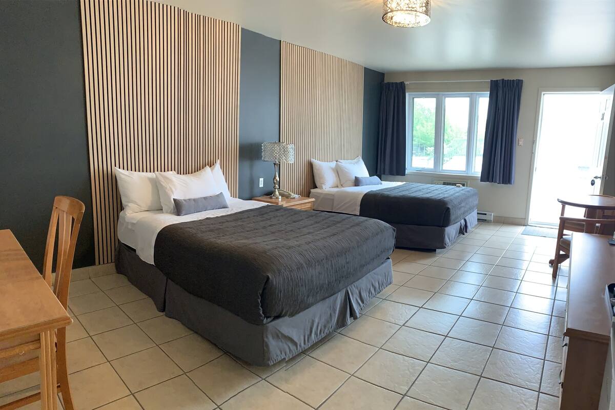 A hotel room with two beds, a dining table, and a window with curtains.