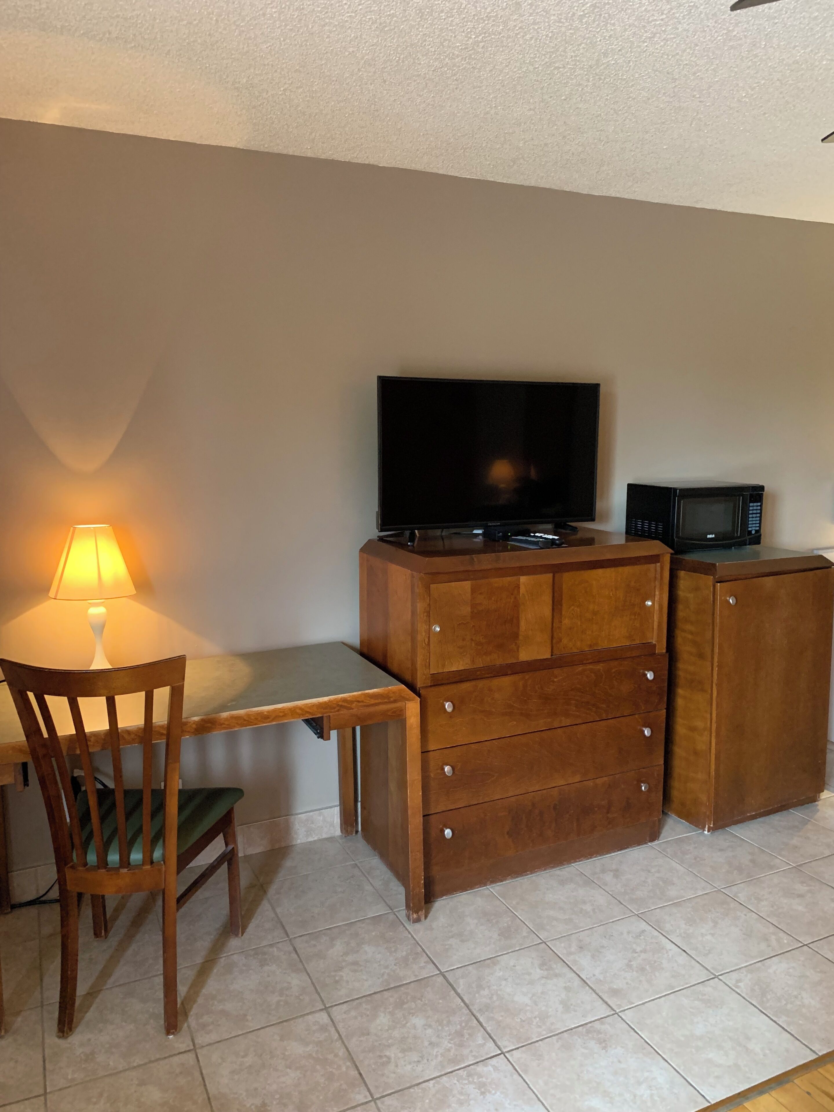 A small room with a wooden desk, a television, a microwave, and a chair.