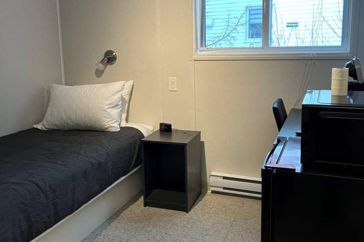 A small, sparsely furnished room with a single bed, a desk, and a window.