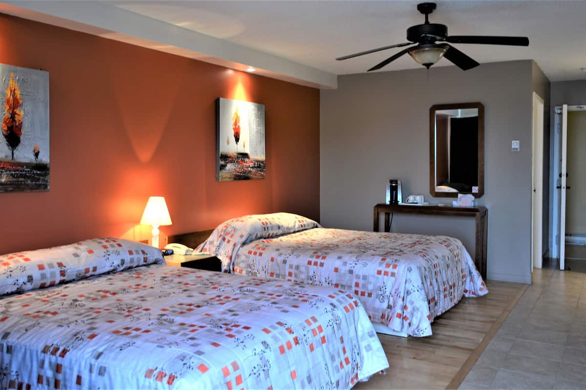 A hotel room with two beds, a ceiling fan, a painting on the wall, a bedside table with a lamp, and a mirror.