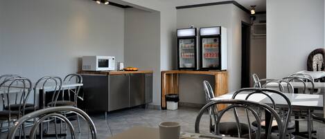 Un restaurante moderno con sillas y mesas de metal, un microondas y dos dispensadores de bebidas.