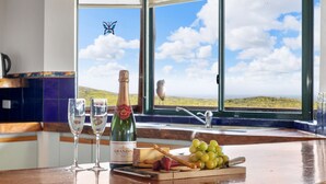 A kitchen counter with a bottle of Grandin Brut, two glasses, a cheese platter, and a view of a landscape through a window. - Red Door - **Spectacular views, close to beach, large spaces** (Gnarabup)