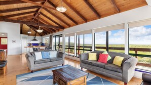 A spacious living room with two grey sofas, a wooden coffee table, and large windows offering a view of the countryside. - Red Door - **Spectacular views, close to beach, large spaces** (Gnarabup)