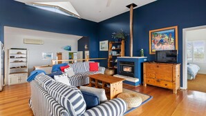 A living room with a fireplace, striped sofas, a wooden coffee table, and a bookshelf. - Tru Blu Beach House - **Beach house, two storey, fully equipped kitchen** (Gracetown)
