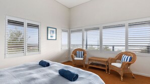A room with a bed, two wicker chairs, a small table, and large windows with blinds. - Tru Blu Beach House - **Beach house, two storey, fully equipped kitchen** (Gracetown)