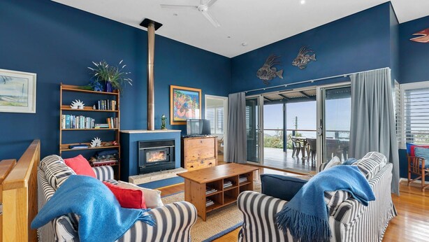 A living room with a fireplace, a bookshelf, a sofa, and a view through a glass door. - Tru Blu Beach House - **Beach house, two storey, fully equipped kitchen** (Gracetown)