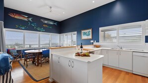 A modern kitchen with white cabinets, a central island, and a dining area with blue chairs. - Tru Blu Beach House - **Beach house, two storey, fully equipped kitchen** (Gracetown)