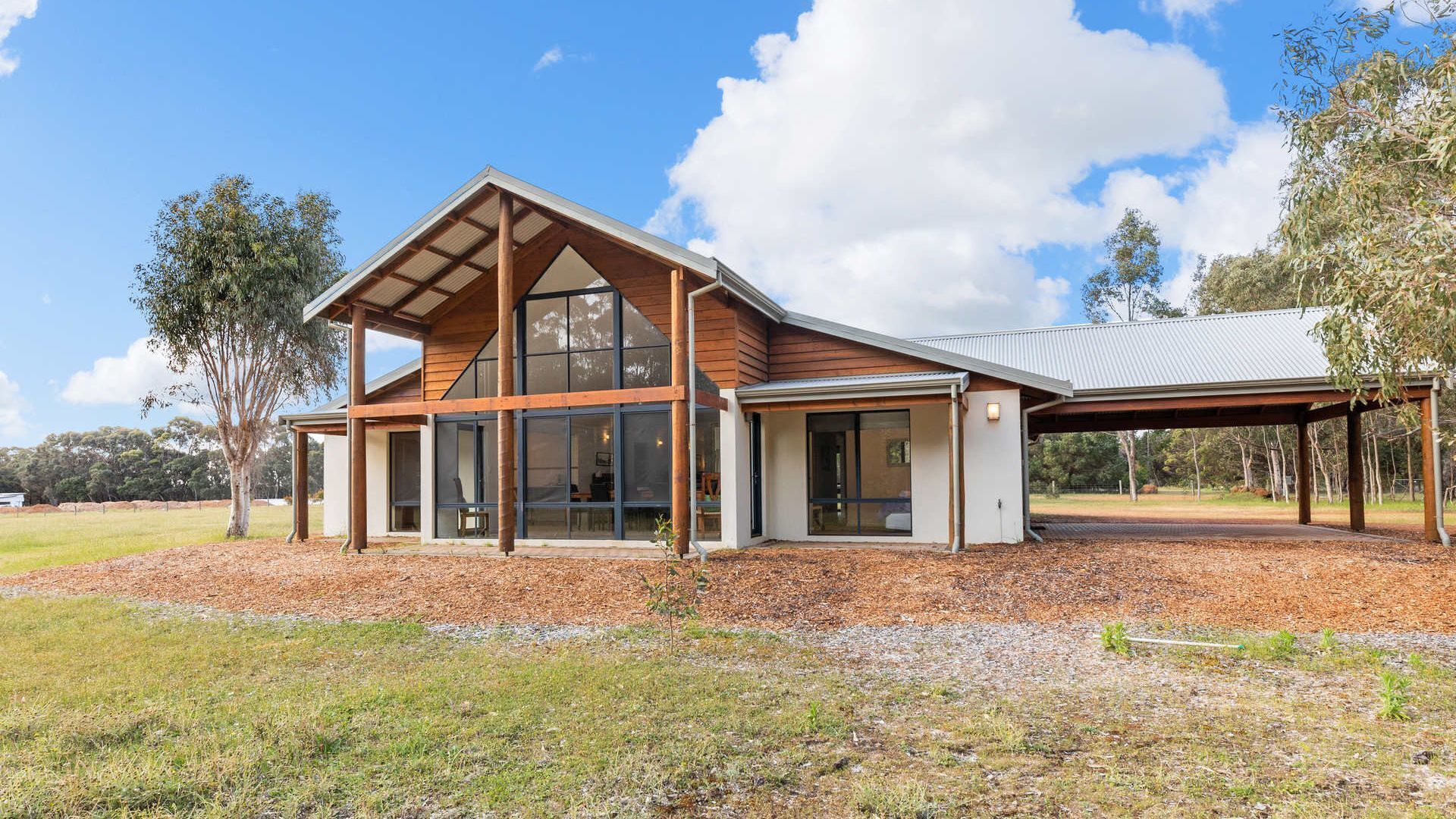 Une maison moderne dotée de grandes fenêtres, d’un espace extérieur couvert et s’intégrant dans un paysage naturel.