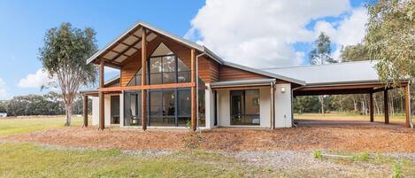 Une maison moderne dotée de grandes fenêtres, d’un espace extérieur couvert et s’intégrant dans un paysage naturel.