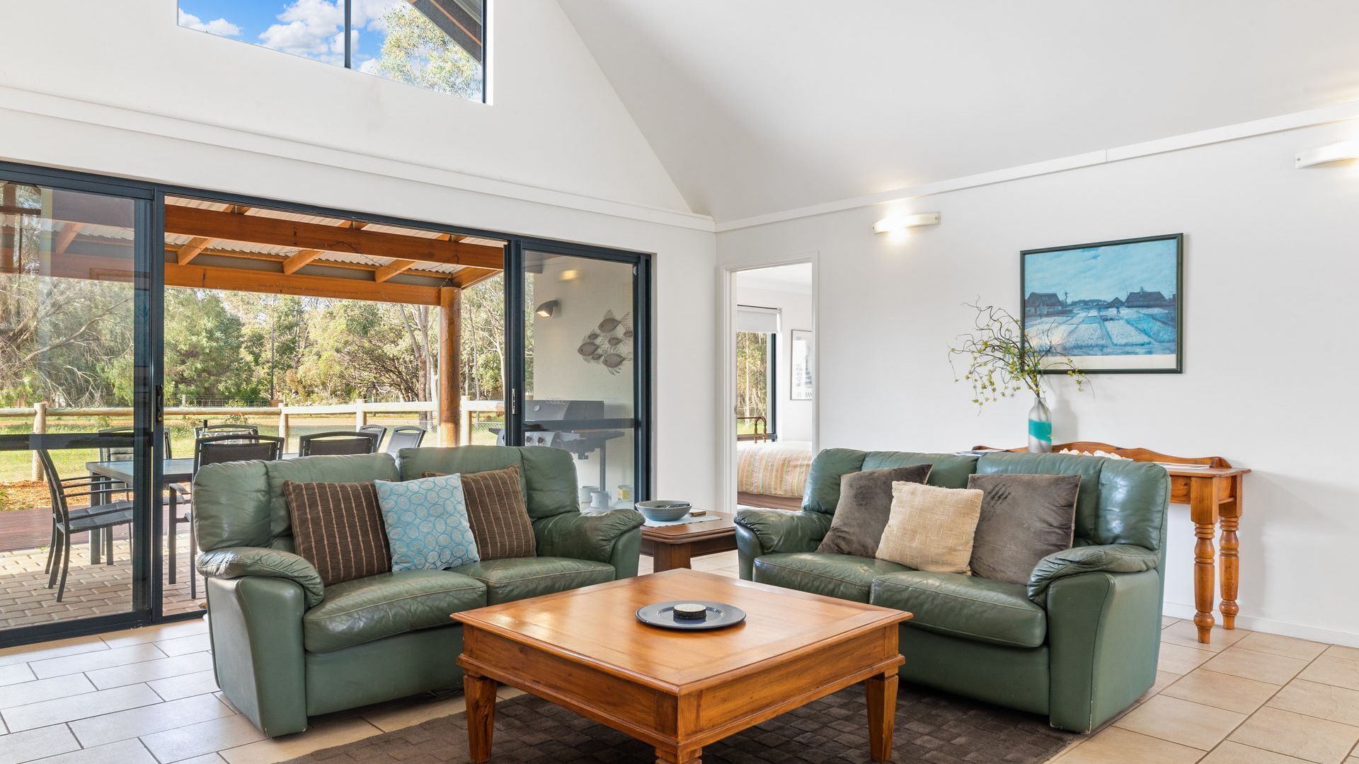 A spacious living area with a green leather sofa set, a wooden coffee table, and a large sliding glass door leading to an outdoor patio.