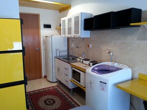 A compact kitchen with a refrigerator, stove, microwave, and a washing machine. - Studio de Casal no Brás  (Brás)