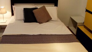 Ein ordentlich bezogenes Bett mit dunkelbraunem Kopfteil, weißen Leinentüchern und einer braunen Tagesdecke.