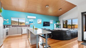 A modern kitchen with a large island, a dining area with a black leather couch, and a view of the landscape through large windows. - Beachside at Margaret River (Prevelly) - Modern beach house, ocean views, spacious interior, reverse (PREVELLY)