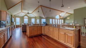 Una cocina amplia con armarios de madera, una isla grande y vistas al océano a través de ventanas panorámicas.