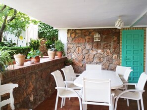 A patio area with a stone wall, white chairs, a round table, and potted plants.