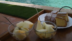 Una mesa con un plato de postres y cuencos de fruta al lado de una piscina.