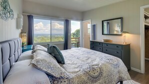 A bedroom with a large bed, a dresser, a mirror, and a view of the outdoors.