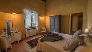 A bedroom with a large bed, a dresser, a chair, a wardrobe, and a window with curtains. - Romignano wine farm. Your villa in TUSCANY. (Traiana)