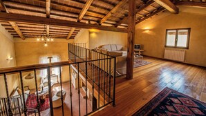 A spacious loft with a high ceiling, wooden beams, a staircase, a sofa, a television, and a window. - Romignano wine farm. Your villa in TUSCANY. (Traiana)
